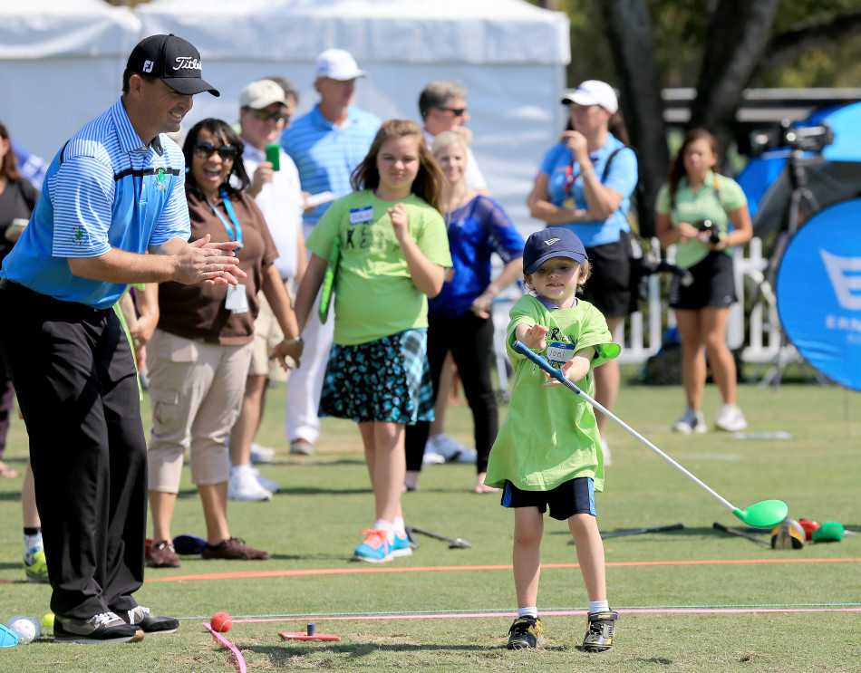 查尔默斯单膝跪地，与一位矮小的孩子平视，细致地调整他的手腕角度。