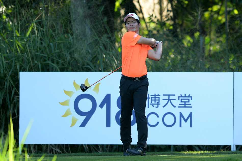 梁文冲身着亮眼橘色球裤，在球道上自信挥杆，阳光勾勒出他专注的侧影