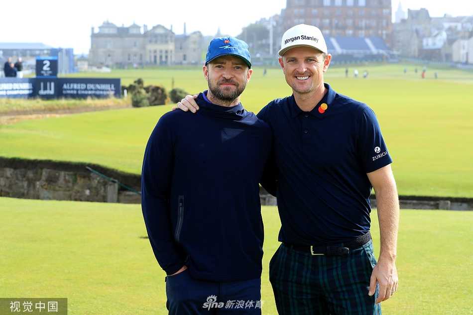 贾老板汀布莱克在老球场练习果岭旁，面带标志性笑容，轻松推杆，背后是古老的圣安德鲁斯小镇建筑。