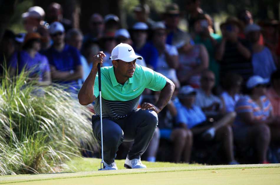 伍兹在果岭上俯身轻抚草皮，细腻感受坡度与草纹，为推杆做最后准备