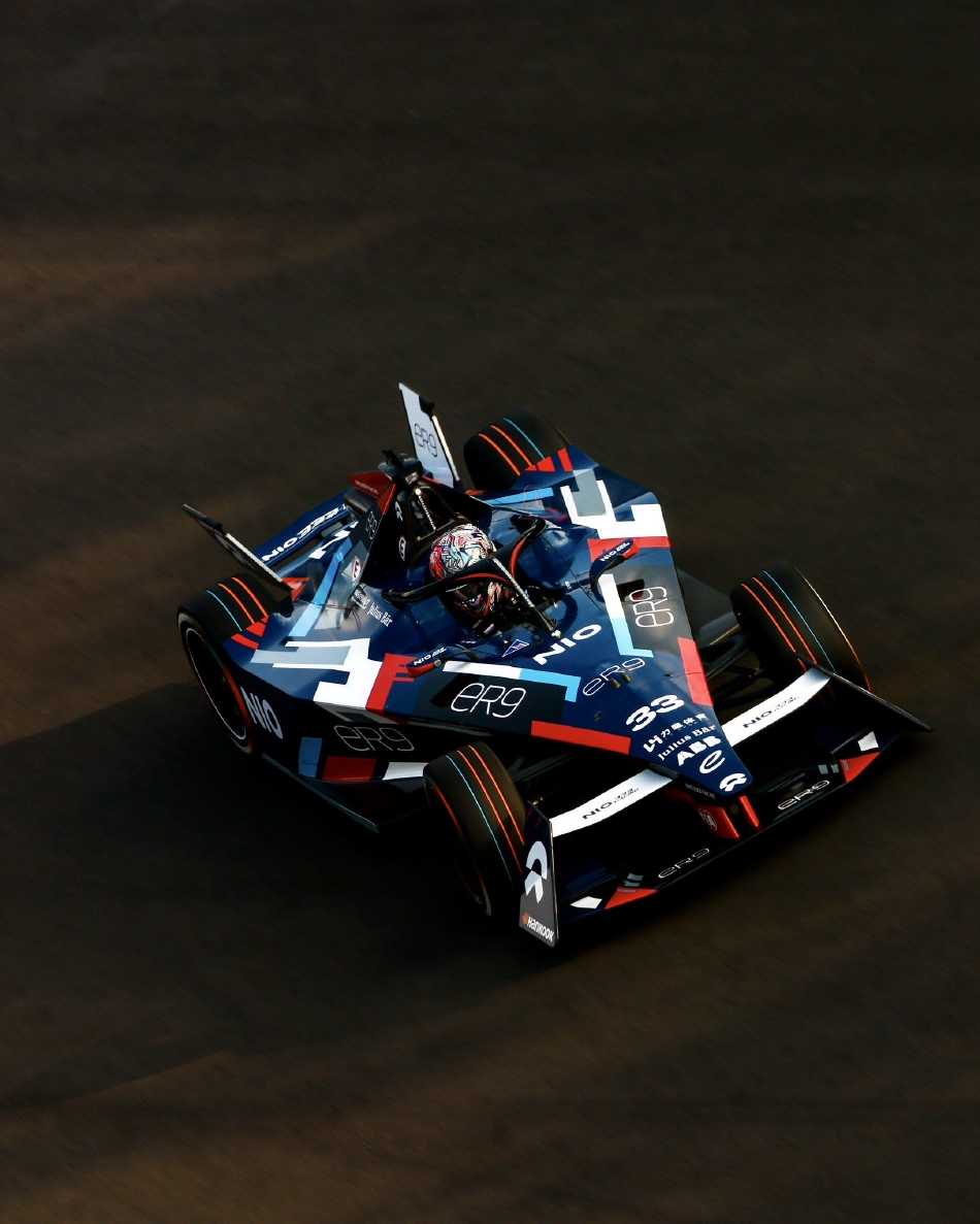 车手头盔紧贴座舱，护目镜映出赛道围栏与蓝天，专注的目光穿透镜面，仿佛已锁定前方即将挑战的连续弯角。