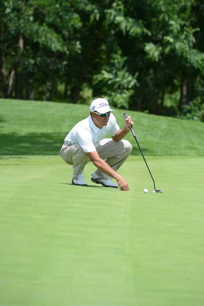 选手在果岭上凝神推杆，背景是开阔的球场，展现了这项运动的宁静与专注